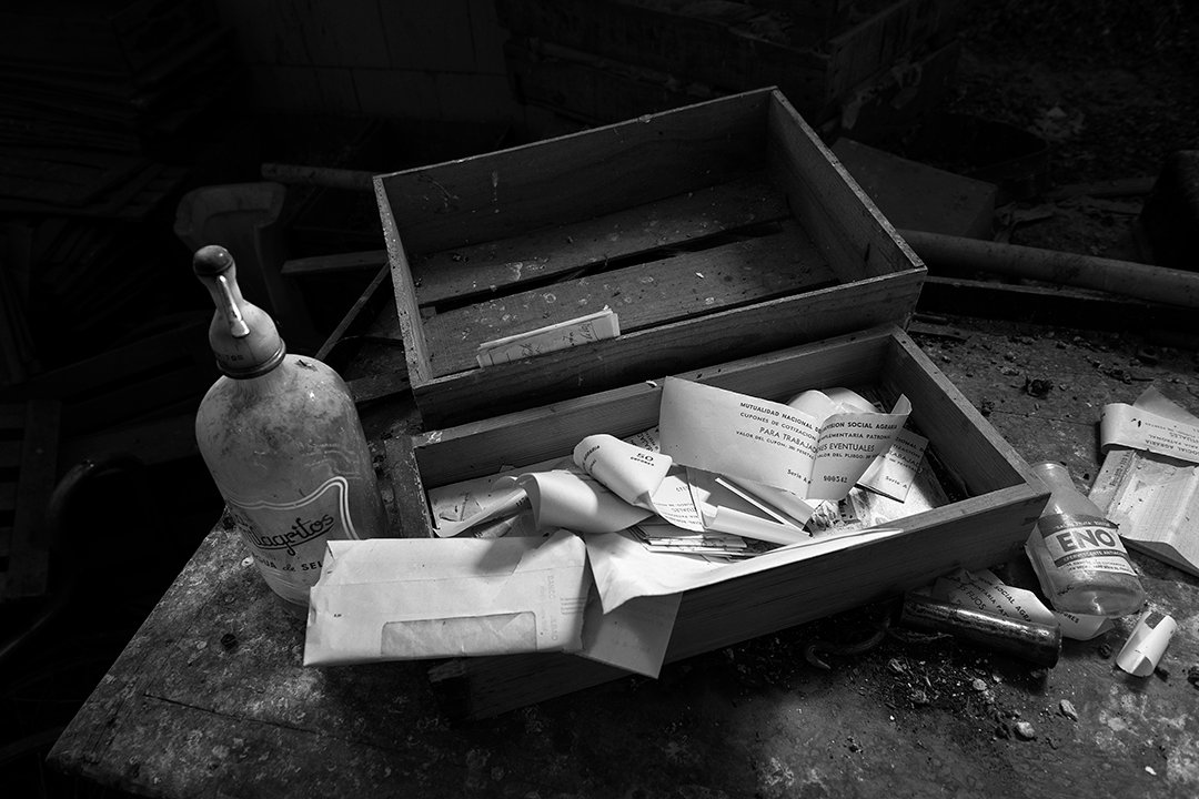 A drawer with papers and a bottle among abandoned objects.